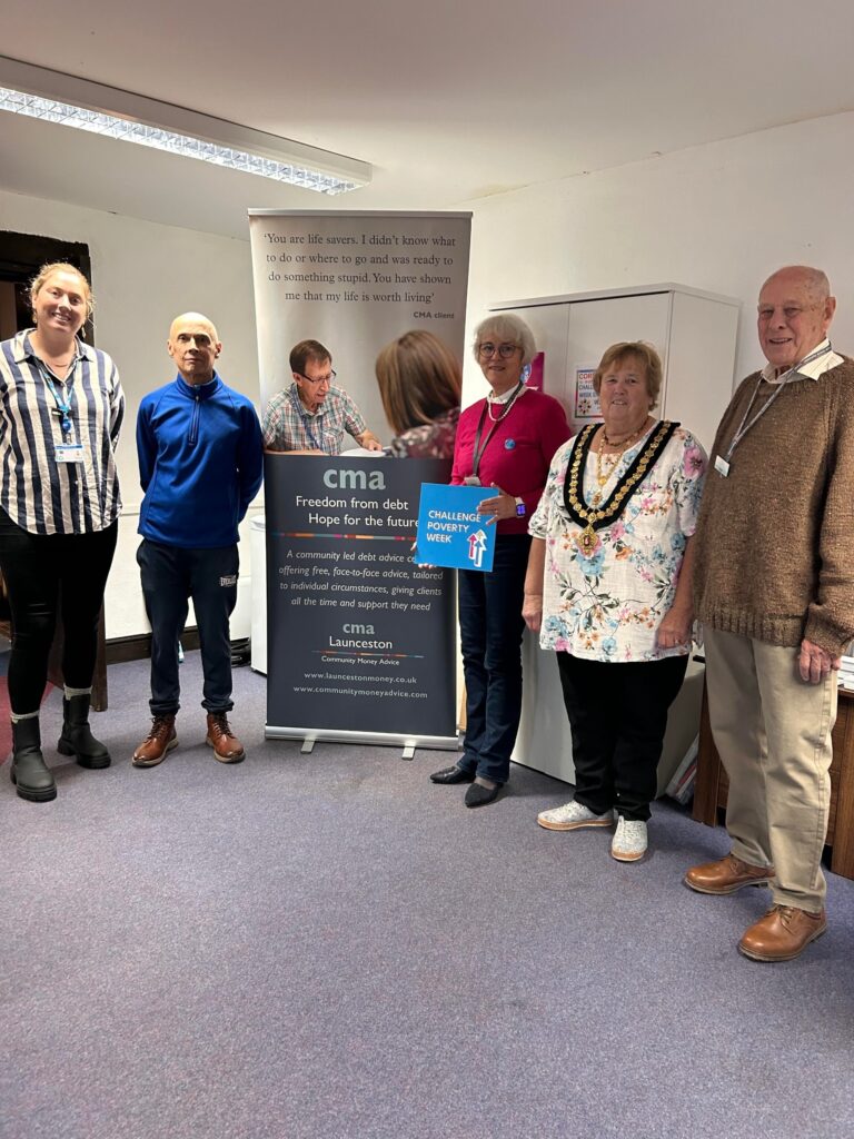 CMA Launceston team and guests at the Challenge Poverty Week coffee morning, standing beside the CMA Launceston banner, one holding a Challenge Poverty Week sign